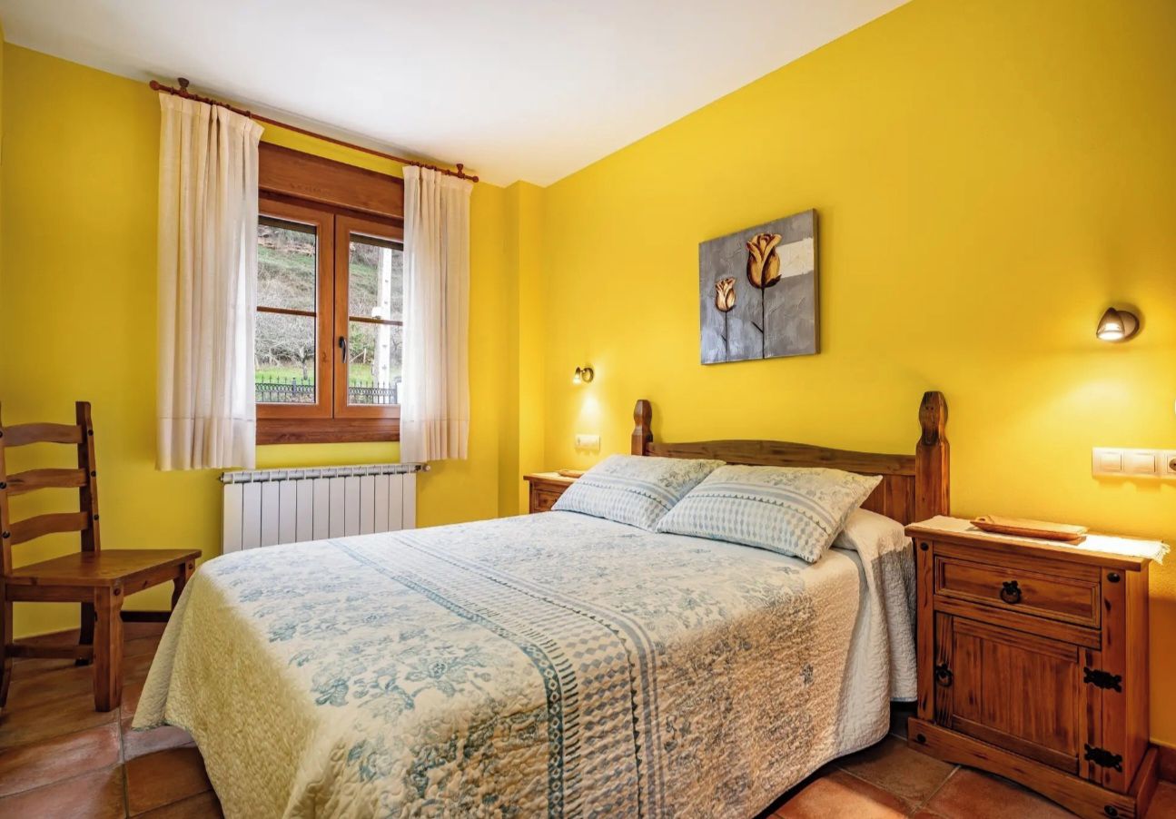 Un dormitorio con una cama, una silla de madera, una mesita de noche y una ventana con cortinas.