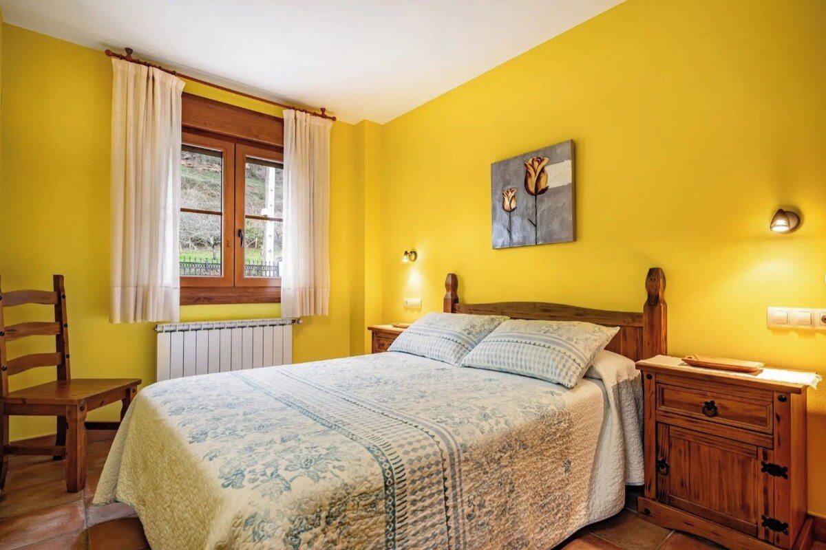 A bedroom with a bed, a wooden chair, a nightstand, and a window with curtains.