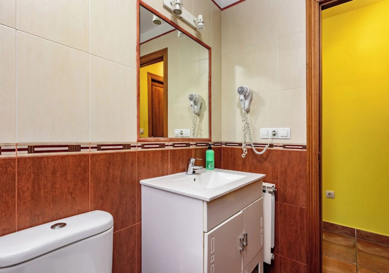 A bathroom with a white sink, mirror, and two hair dryers mounted on the wall.