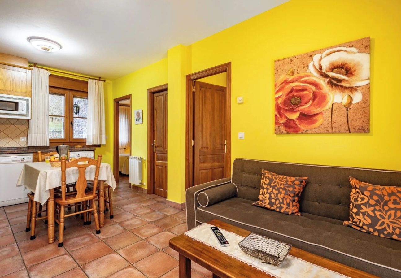 A living room with a sofa, a dining table with chairs, a kitchen area, and a door.