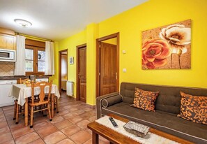 A living room with a sofa, a dining table with chairs, a kitchen area, and a door.