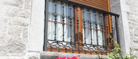 A stone building with a window featuring a wooden shutter and decorative metal bars.