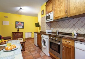 A compact kitchen with a washing machine, oven, microwave, and wooden cabinets. - Apartamentos Rurales La Viña (Cangas de Onis)