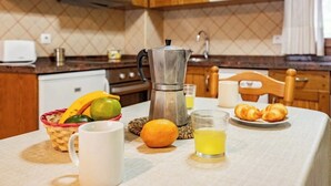 Ett kök med träskåp, en kaffebryggare, en fruktskål, en tallrik med croissanter och ett glas juice.