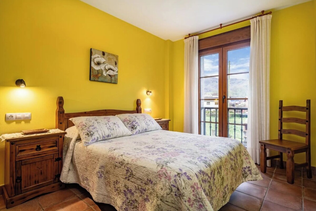 A bedroom with a bed, bedside tables, a chair, a window with curtains, and a wall-mounted light fixture.