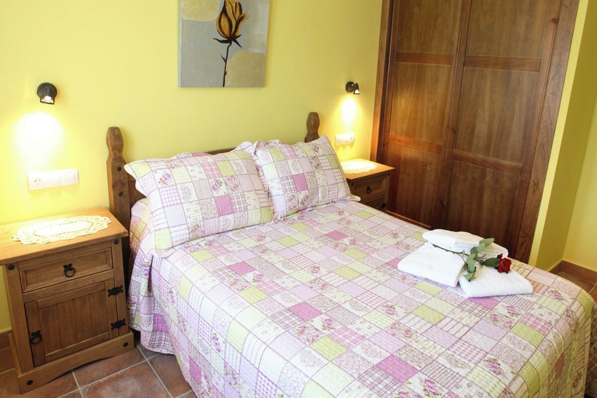 A bedroom with a bed, nightstands, a wooden wardrobe, and a wall-mounted light fixture.