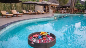 A poolside area with lounge chairs and a floating basket with fruits and a drink. - Toyam By Orchid Hotels (Bhor)