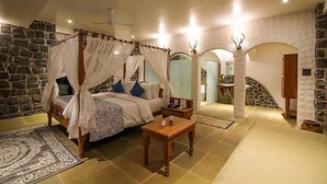 A four-poster canopy bed with a stone wall backdrop, a wooden nightstand, and a patterned rug. - Toyam By Orchid Hotels (Bhor)