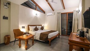 A hotel room with a bed, a desk, a chair, a ceiling fan, and a sliding glass door. - Toyam By Orchid Hotels (Bhor)