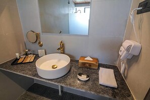 Un baño con un lavabo redondo, un espejo, una toalla, un secador de pelo y un jabonera.