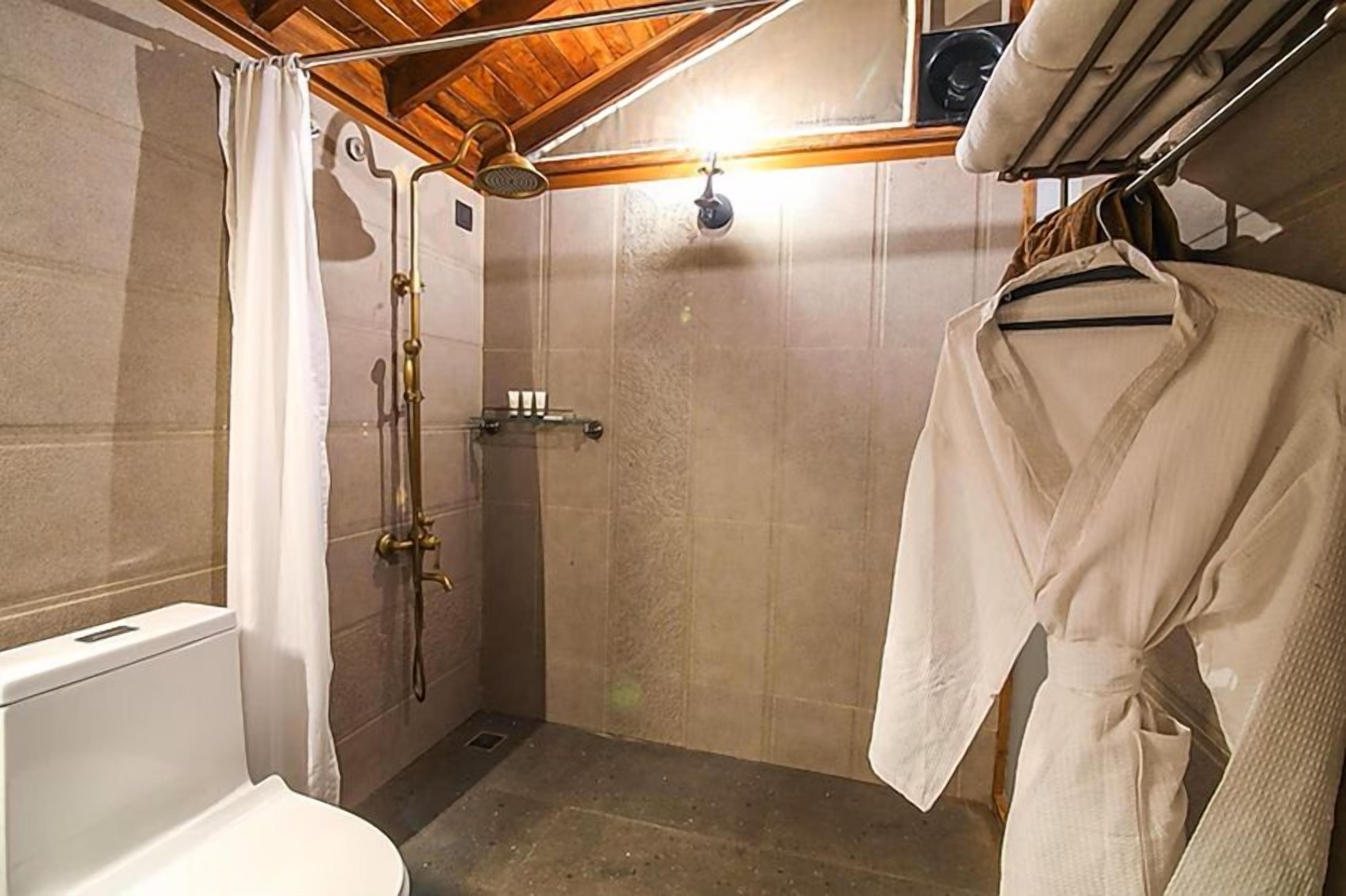 A small, compact bathroom with a shower, toilet, and a drying rack with a robe.