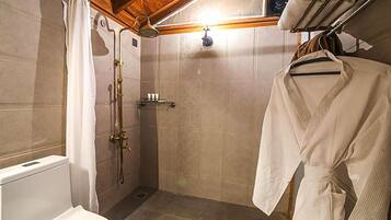 A small, compact bathroom with a shower, toilet, and a drying rack with a robe.