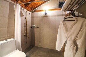 Een kleine, praktische badkamer met douche, toilet en een droogrek met een badjas.