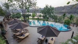 A pool area with lounge chairs and umbrellas, surrounded by trees and a view of hills. - Toyam By Orchid Hotels (Bhor)