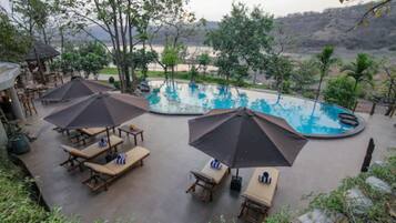 A pool area with lounge chairs and umbrellas, surrounded by trees and a view of hills.