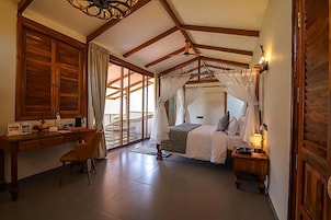 Un dormitorio con cama, escritorio y silla. Hay una ventana con cortinas y vistas al exterior.