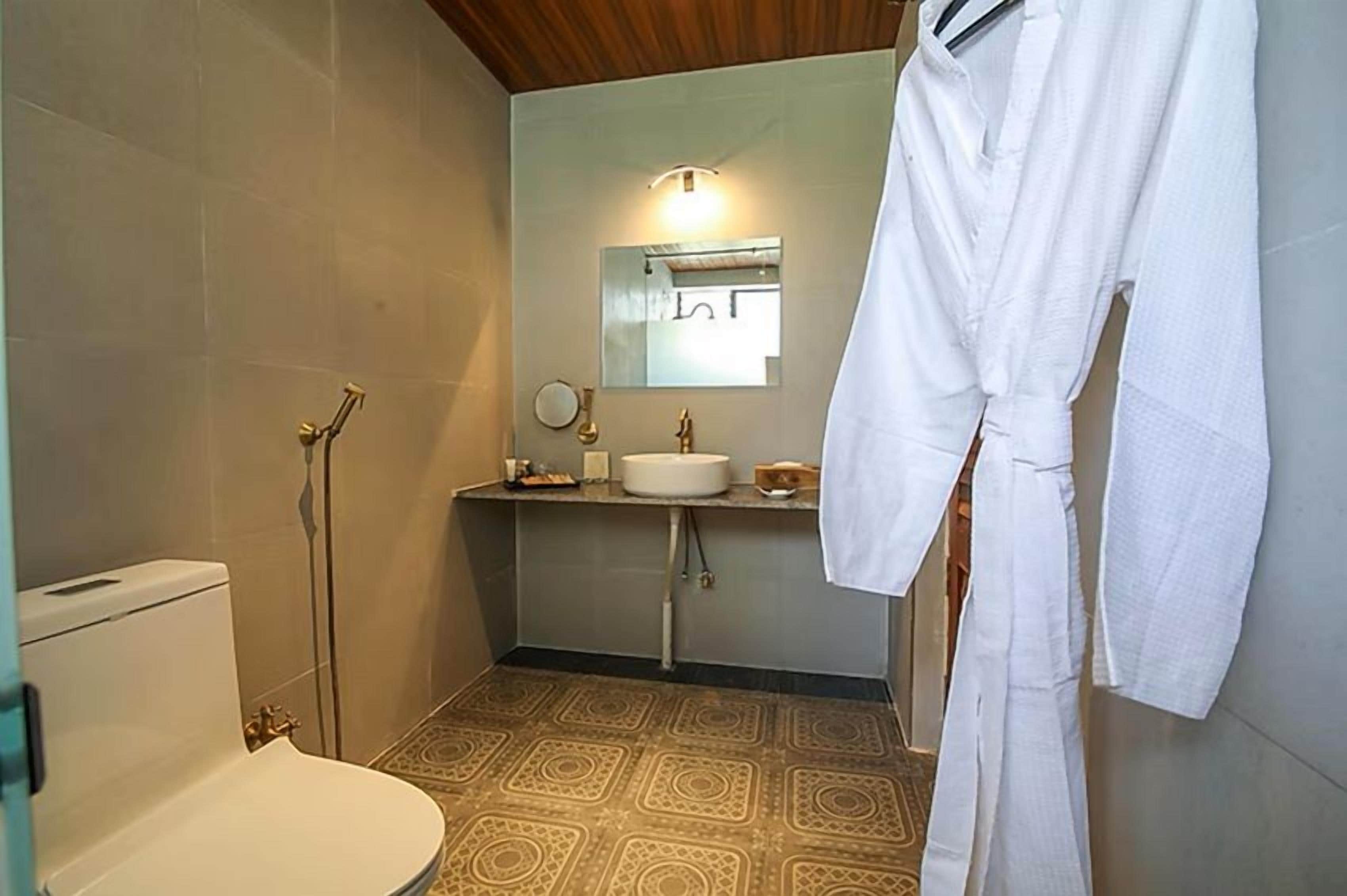 A bathroom with a toilet, sink, and shower. A white robe hangs on the wall.