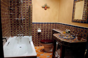 Une salle de bain avec une baignoire blanche, des toilettes et un lavabo, le tout agrémenté d’un mur recouvert de carreaux colorés.