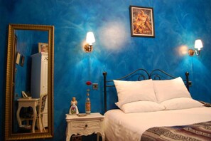 A bedroom with a bed, a nightstand, a mirror, and wall sconces.