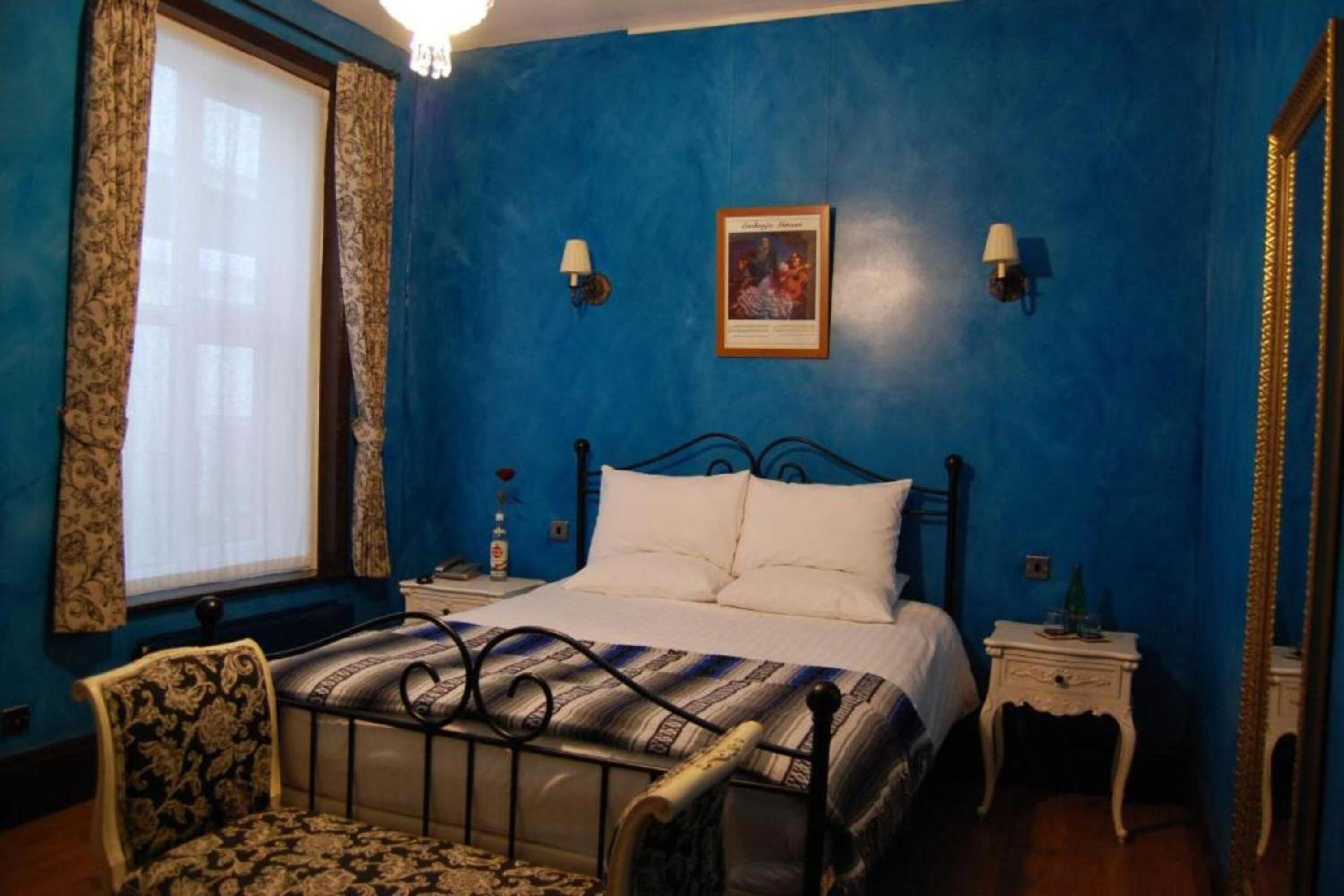 A bedroom with a bed, a chair, a nightstand, a lamp, and a wall-mounted picture.
