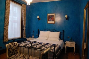 Une chambre à coucher comprenant un lit, une chaise, une table de chevet, une lampe et un tableau accroché au mur.