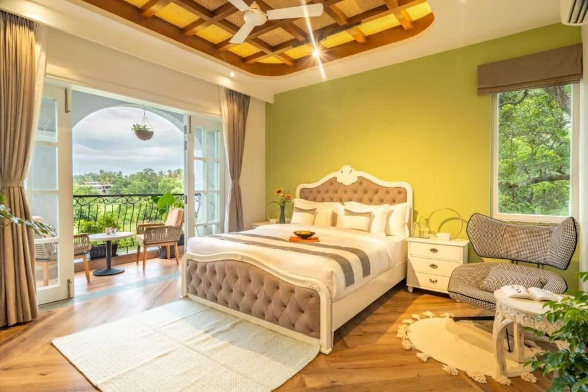 A bedroom with a bed, a nightstand, a chair, a window, and a balcony.