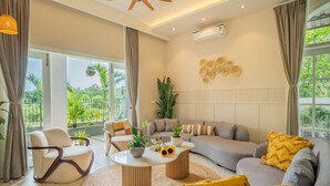 A modern living room with a sofa, armchairs, a coffee table, and a ceiling fan. - Elivaas Vacasa - Goa (Candolim)