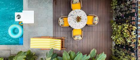 A poolside area with a round table, yellow cushions, a striped towel, and potted plants.