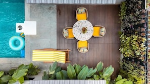 A poolside area with a round table, yellow cushions, a striped towel, and potted plants. - Elivaas Vacasa - Goa (Candolim)
