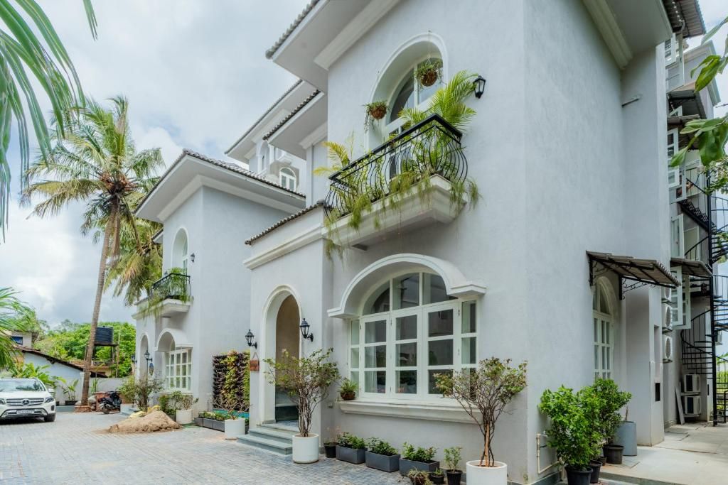 A white building with arched windows and balconies with plants.