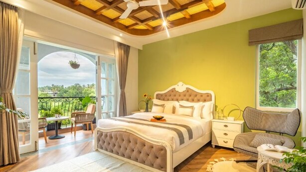 A bedroom with a bed, a nightstand, a chair, a window, and a balcony. - Elivaas Vacasa - Goa (Candolim)