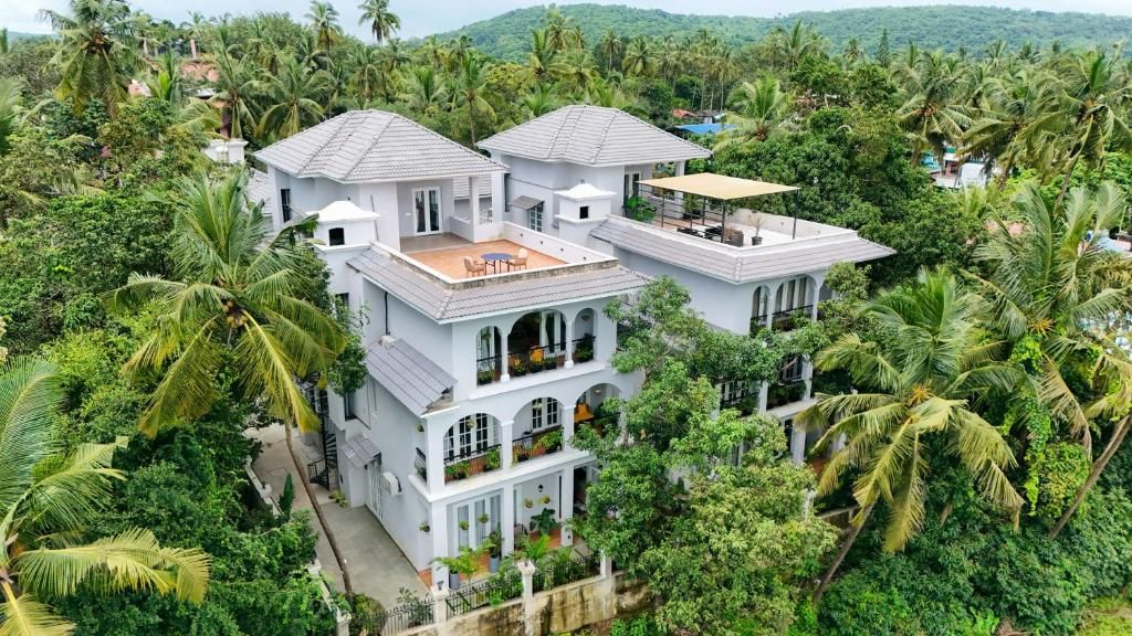 A multi-story white building with a flat roof, surrounded by dense greenery and palm trees.