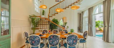 A dining area with a wooden table and chairs, a staircase, and a view of a pool.