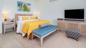 Un dormitorio con cama, mesitas de noche, un banco y una televisión, además de un banco de ratán.