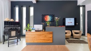 A modern reception area with a wooden desk, two chairs, a piano, and a wall-mounted TV displaying 'ayuda' logo. - Ayuda Sanctuary Boutique Negombo (Negombo)