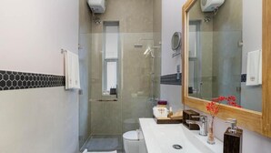 A modern bathroom with a glass shower enclosure, a white sink with a mirror above it, and a small vanity area with toiletries. - Ayuda Sanctuary Boutique Negombo (Negombo)