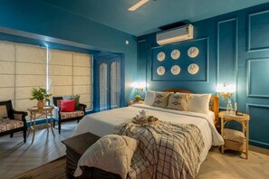 A bedroom with a large bed, a small table with a tray, a chair, and a window with curtains. - Elivaas Bludoor - Goa (Assagao)