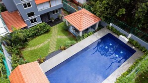 A swimming pool with a tiled deck, surrounded by greenery and a small gazebo. - Elivaas Bludoor - Goa (Assagao)