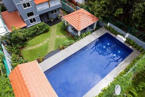 A swimming pool with a tiled deck, surrounded by greenery and a small gazebo. - Elivaas Bludoor - Goa (Assagao)
