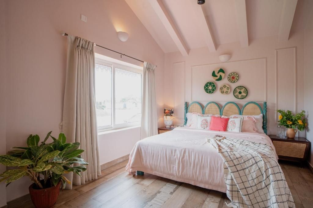 A bedroom with a bed, curtains, a potted plant, a wall with decorative plates, and a window.