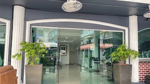 L’entrée d’un hôtel, avec une porte en verre, des plantes en pot et un espace détente avec un fauteuil.