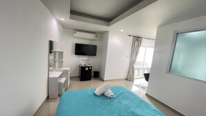 Une chambre d’hôtel moderne équipée d’un lit, d’une télévision, d’un petit bureau et d’une fenêtre avec des rideaux.
