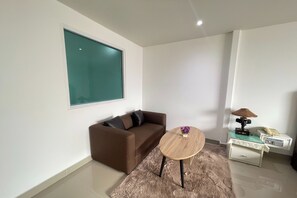 A modern living room with a brown sofa, a round wooden coffee table, a small side table with a lamp, and a large window. - W-9 Hotel By Zuzu (Pattaya)
