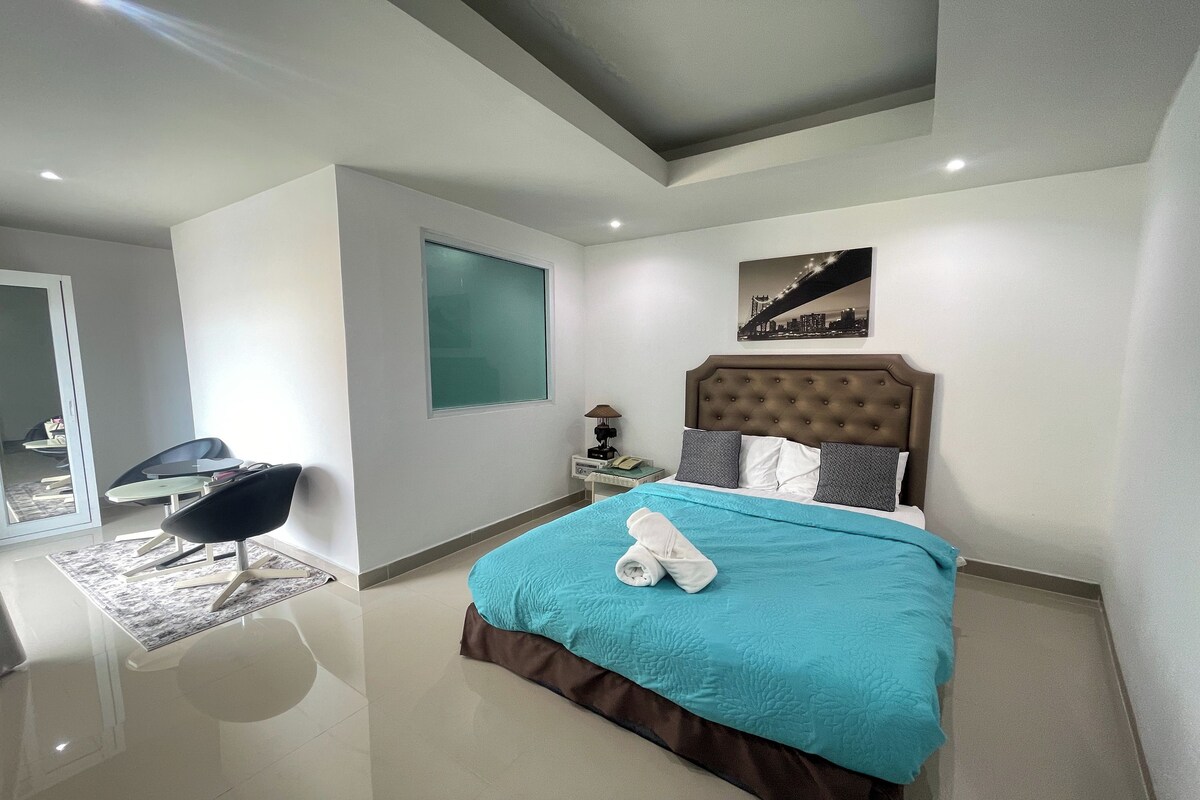A modern bedroom with a large bed, a nightstand, a chair, and a cityscape artwork on the wall.