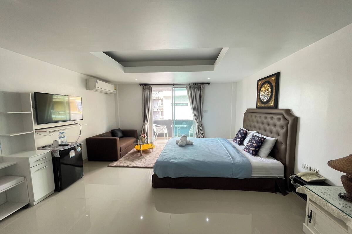 Ein modernes Hotelzimmer mit Bett, Fernseher, Schreibtisch und einer kleinen Küchenzeile.