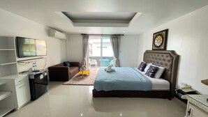 A modern hotel room with a large bed, a flat-screen TV, a desk with a chair, and a small seating area. - W-9 Hotel By Zuzu (Pattaya)