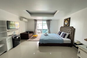 A modern hotel room with a large bed, a flat-screen TV, a desk with a chair, and a small seating area. - W-9 Hotel By Zuzu (Pattaya)
