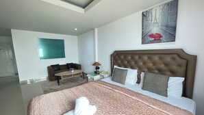 A hotel room with a large bed, a sitting area with a sofa and a small table, and a painting of a rainy street on the wall. - W-9 Hotel By Zuzu (Pattaya)