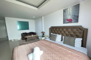 A hotel room with a large bed, a sitting area with a sofa and a small table, and a painting of a rainy street on the wall. - W-9 Hotel By Zuzu (Pattaya)