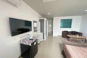 Una habitación de hotel moderna con una televisión de pantalla plana, un escritorio con una botella de agua, un sofá, una mesa de centro y un ventanal grande.